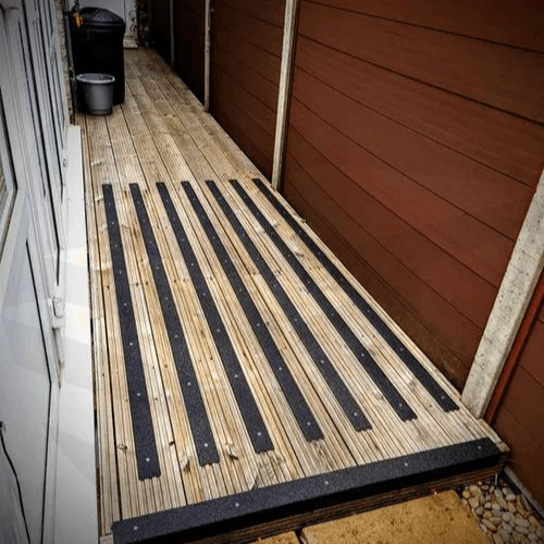 Close-up of black non-slip decking strips installed on wet timber boards.Non Slip Standard GRP Decking Strips black- finishings UK